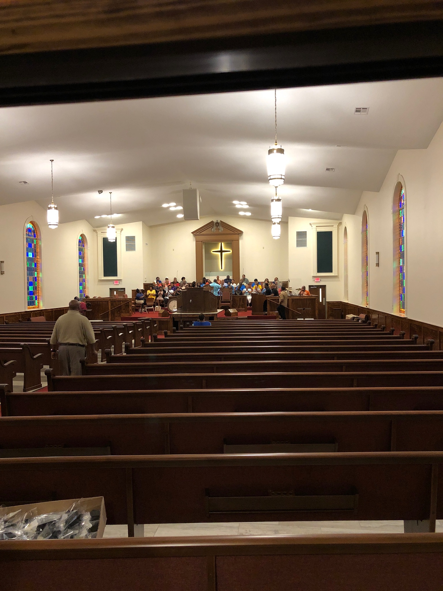 Wide view of the rebuilt Greater Mount Olive sanctuary from the back, showing stained glass arches on both sides, illuminated cross at the front, choir setup at the platform, and Worx Audio loudspeakers hung from the ceiling.