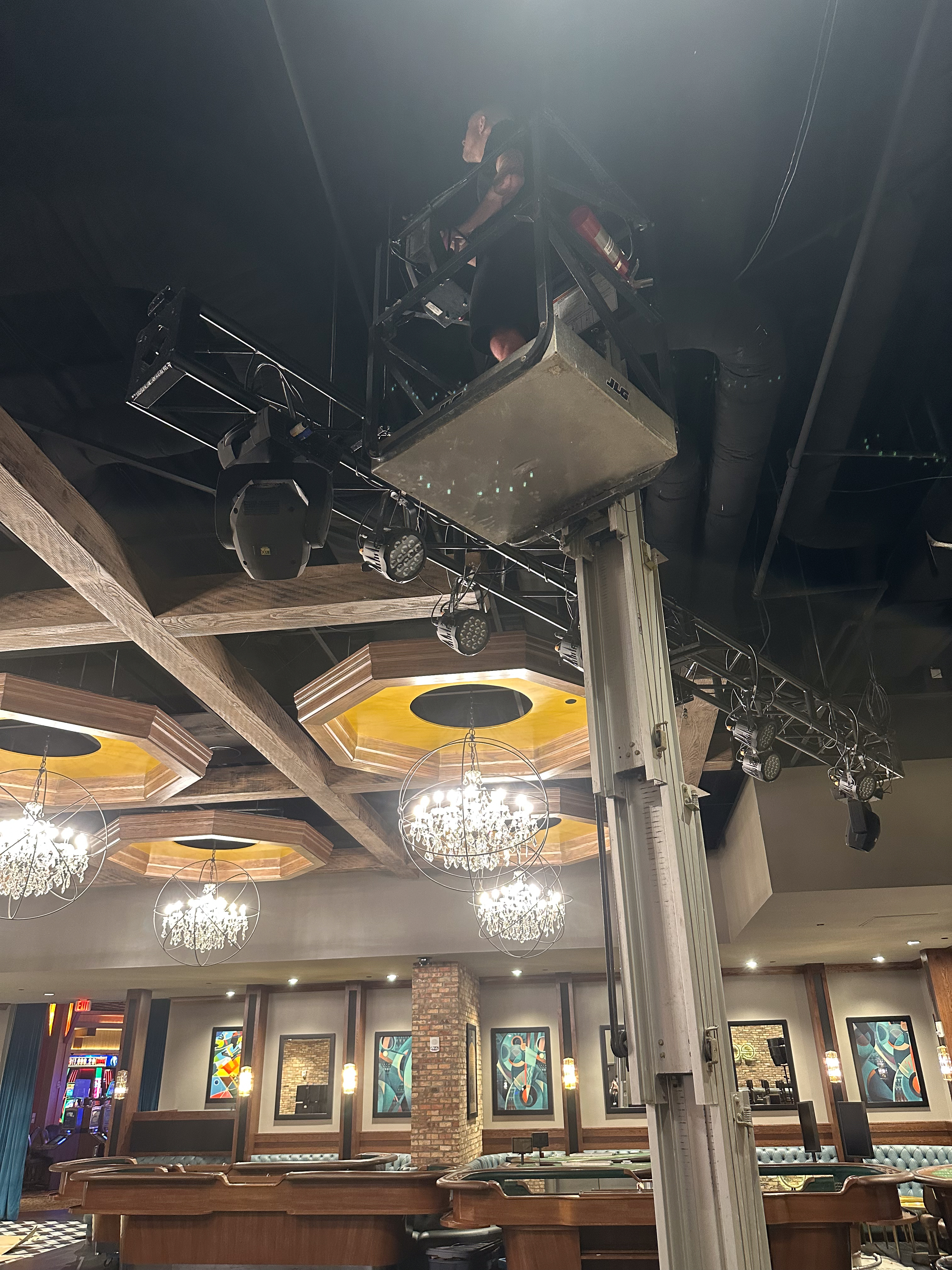 Tech on a scissor lift at full height working on the Panasonic projector mount above the Edge Bar stage.
