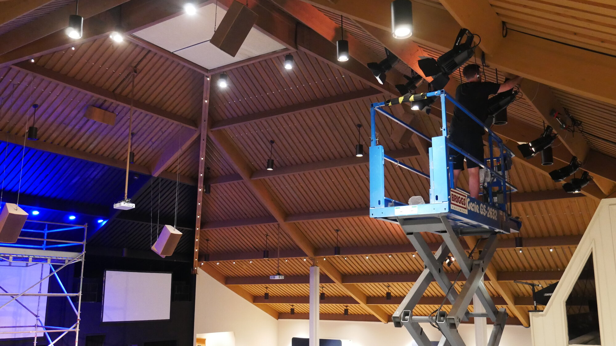 Install in progress at The Chapel — scissor lift extended to the ceiling with a technician hard-mounting a KL Par FC fixture into the wood.