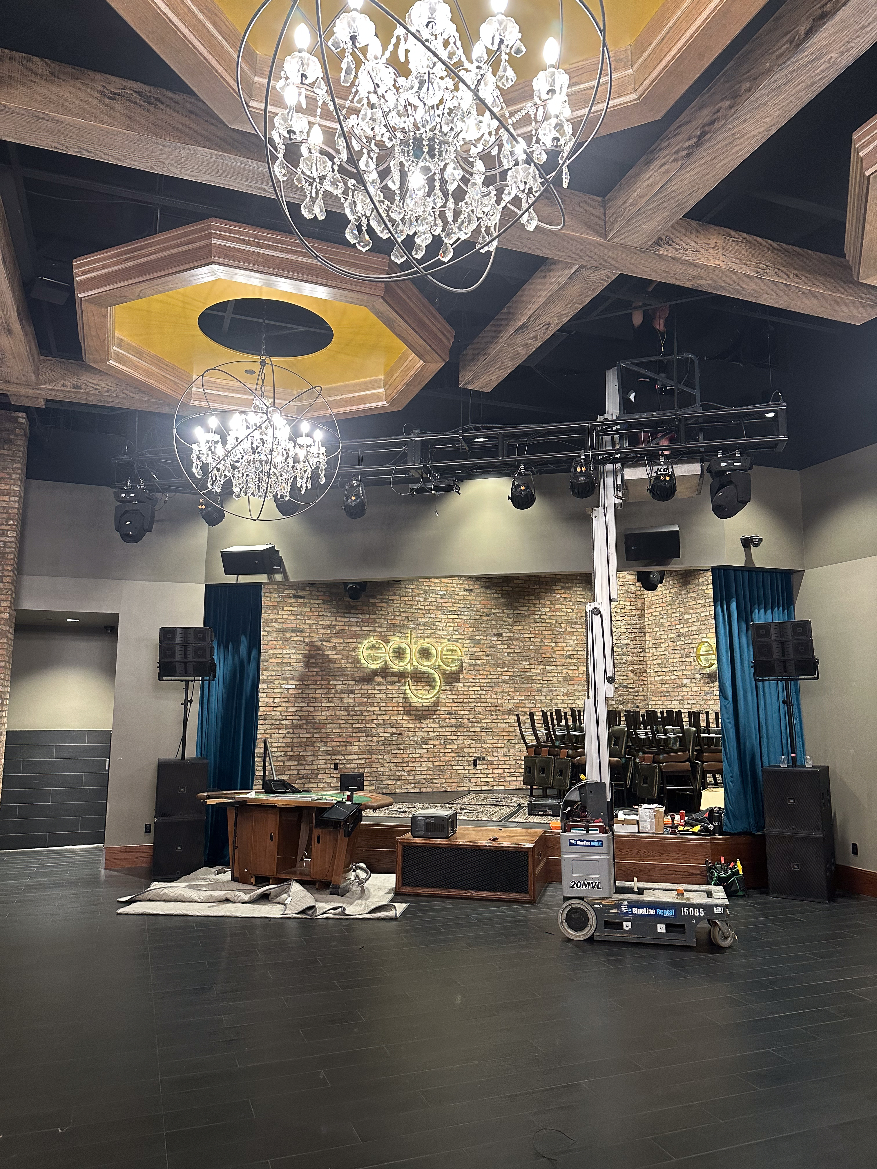 Wide install-day shot of the Edge Bar stage with the projector mounting in progress, scaffold in place, the existing laser rig visible.