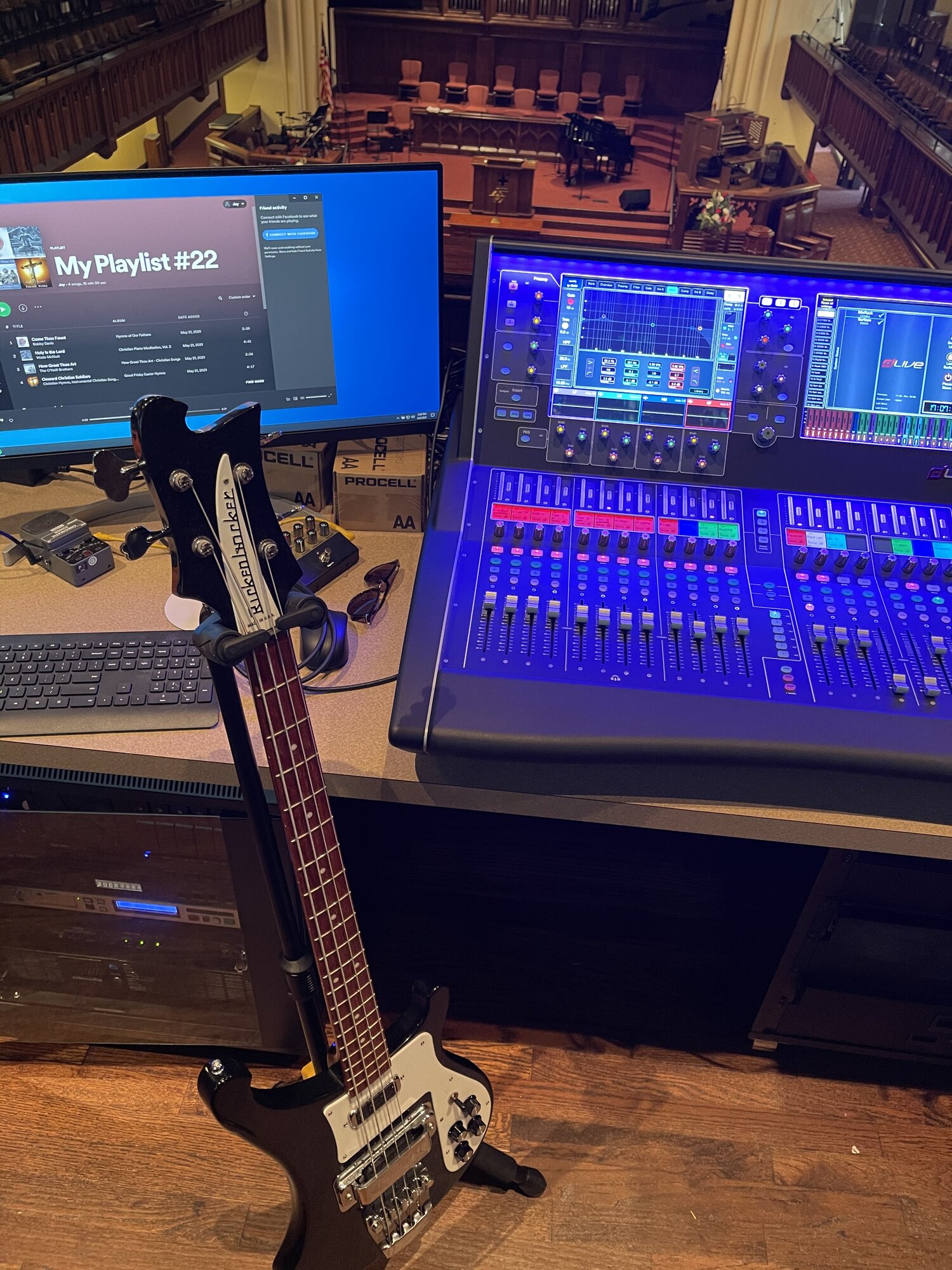 Allen & Heath dLive console at FPCBR front of house with a Rickenbacker bass on a stand, monitor showing the worship team's playlist, and rack-mounted gear below.