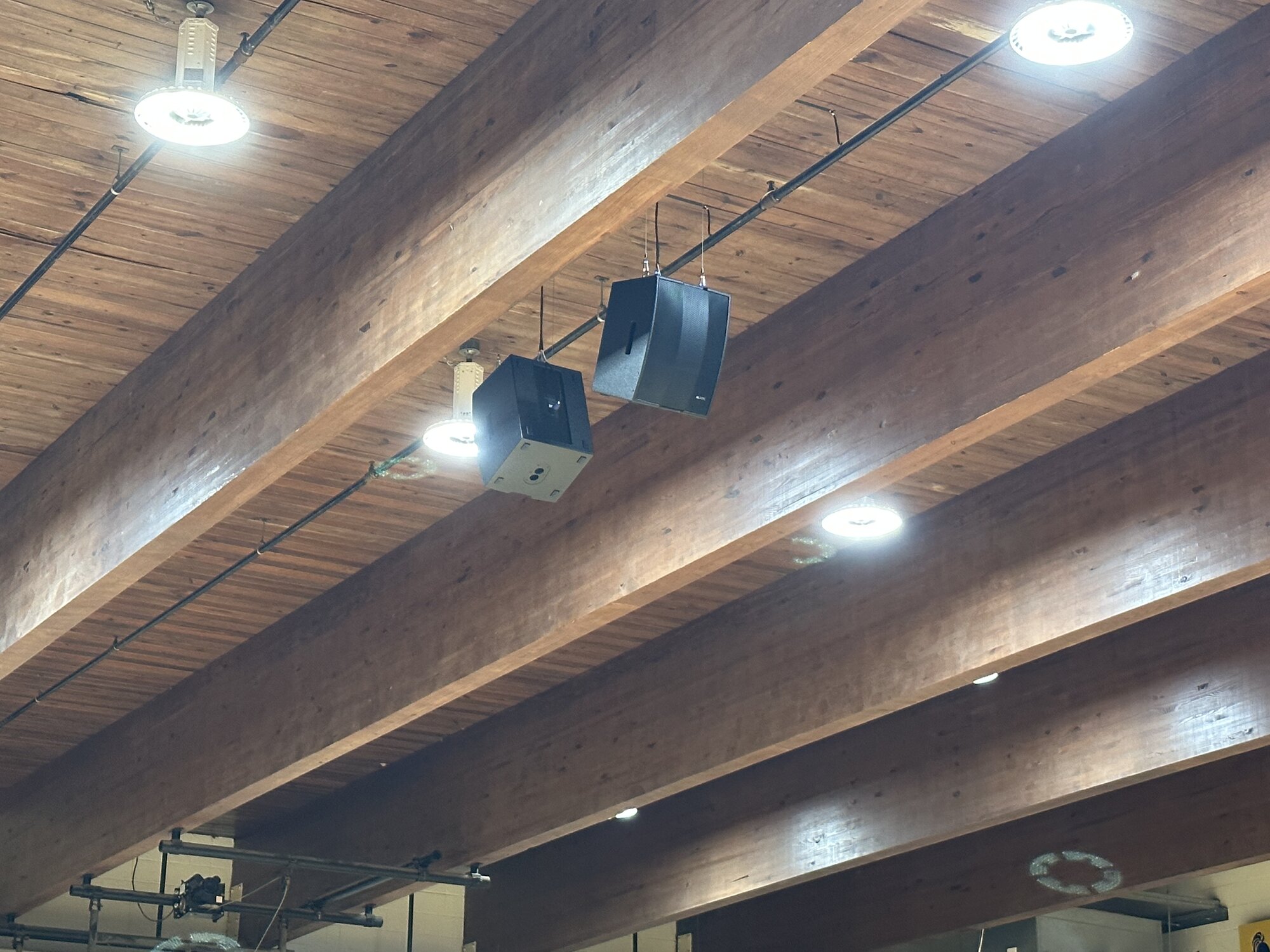 Wide view of the gym from a corner, showing speakers hung between wood beams, championship banners, scoreboard, and the Knights branding.