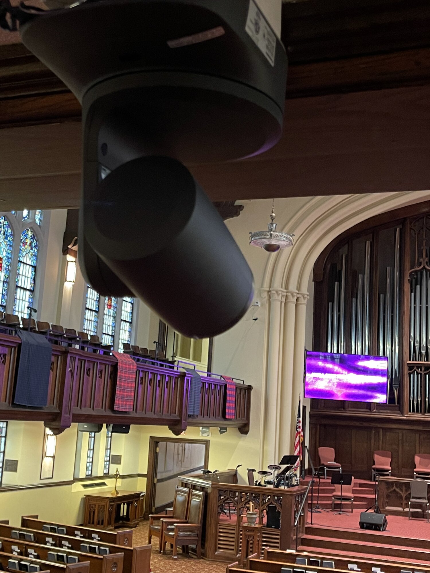 PTZ broadcast camera mounted from the FPCBR balcony ceiling, sanctuary visible below with side IMAG screen showing service graphics.